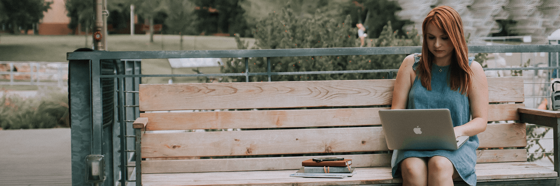Individual sitting on a bench using a laptop.